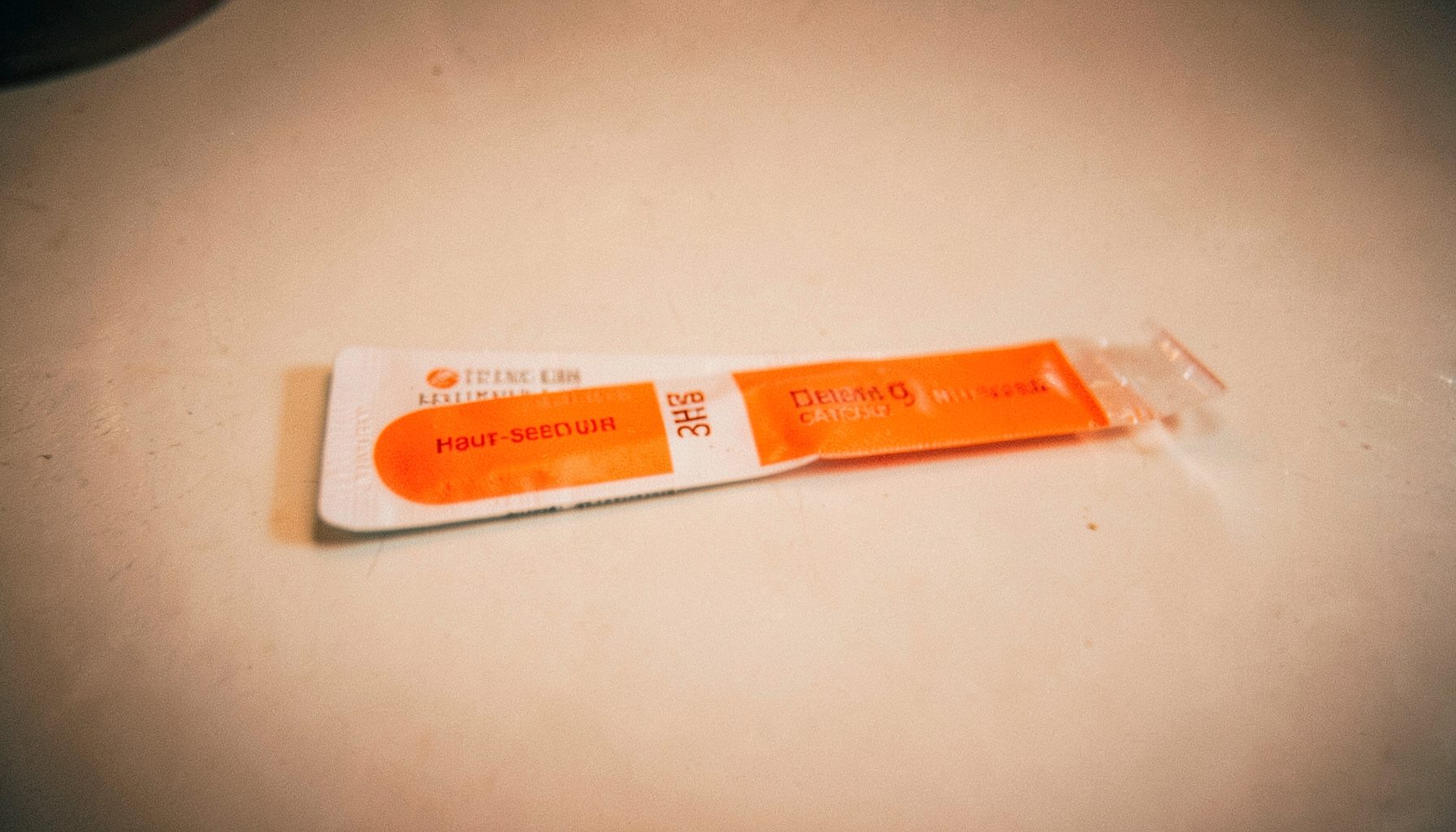 A foil-sealed medication strip with two-tone orange and white branding, soft overhead lighting.