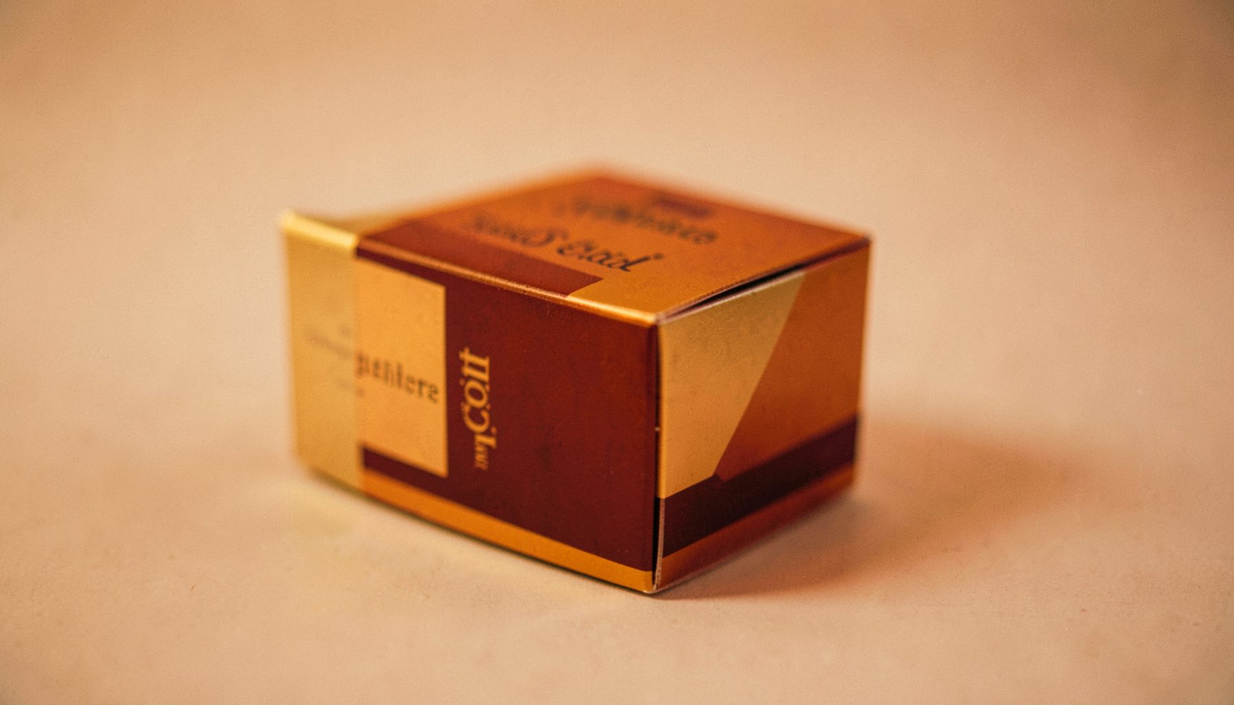 A warm-toned product box with gold and burgundy accents, softly lit on a neutral background.